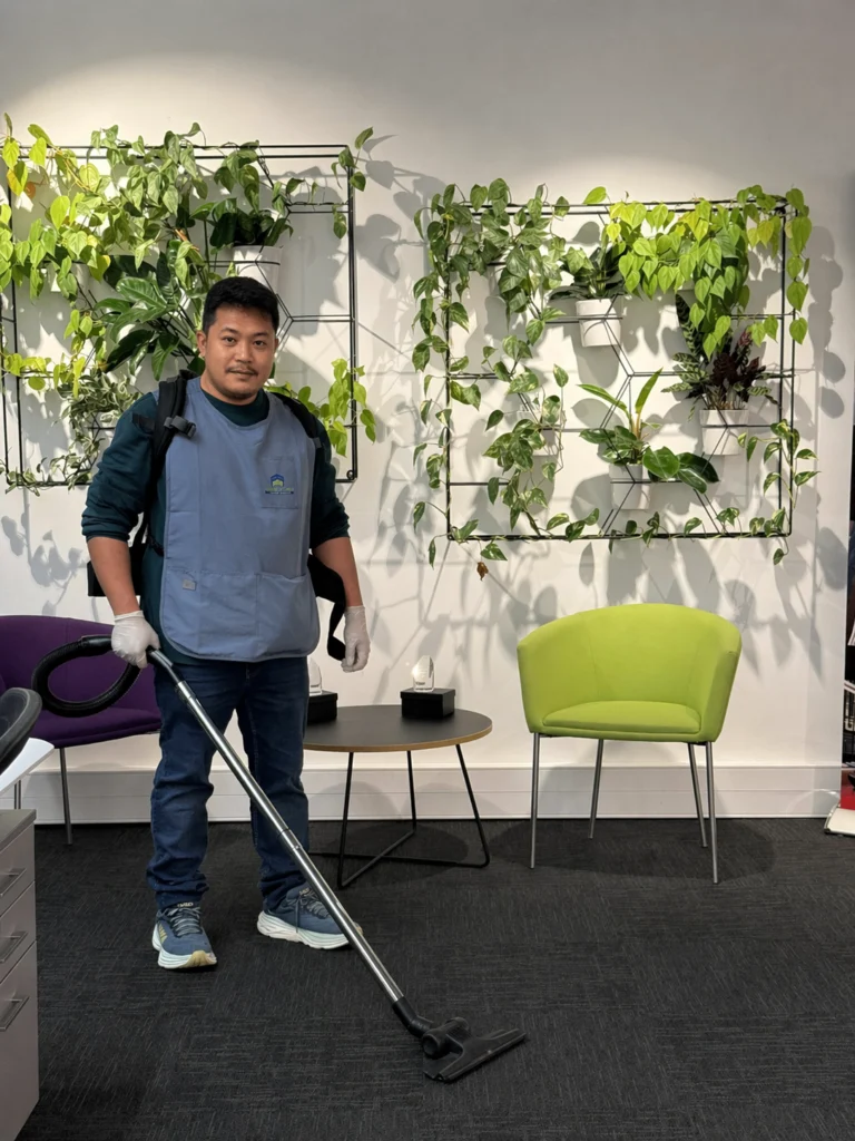 Professional cleaner vacuuming office floor in a modern workspace with plants and seating, maintaining a clean and inviting environment