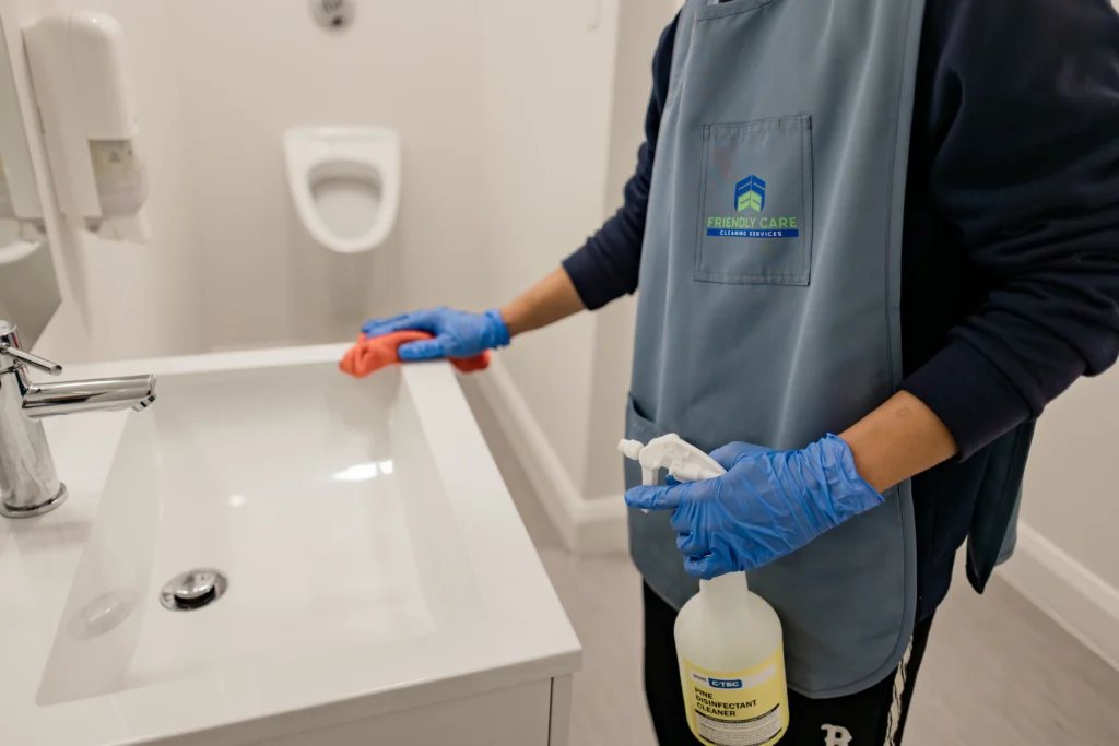 Professional cleaner disinfecting a commercial restroom sink with protective gloves